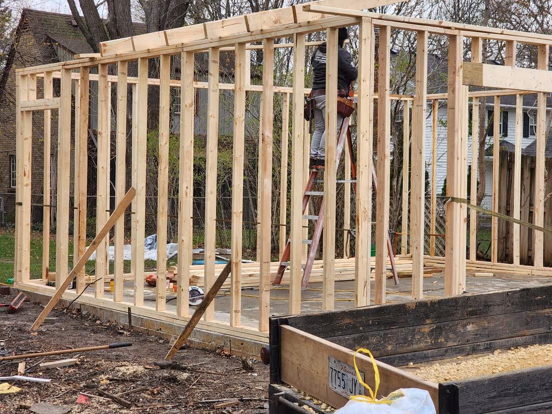Framing of a wooden structure under construction with a worker on a ladder installing beams.