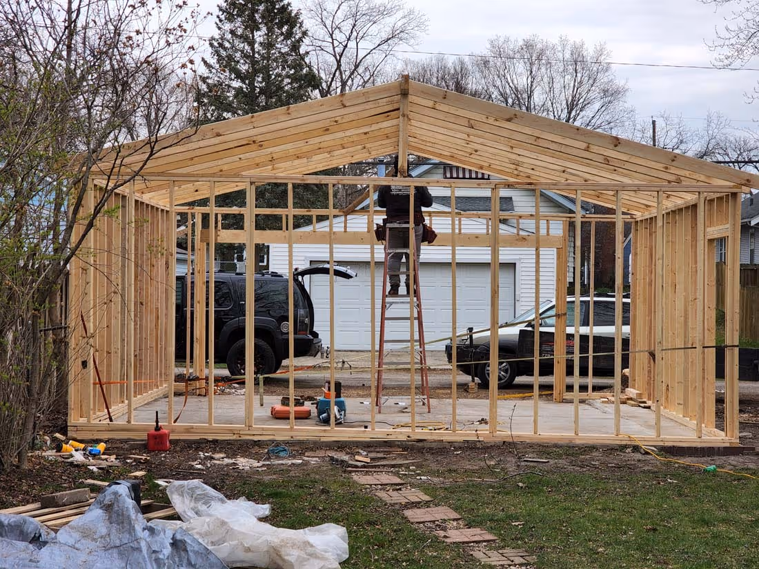 Wooden frame structure of a small building under construction with a person standing on a ladder inside.