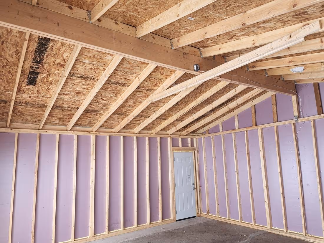 Interior view of an unfinished room with exposed wood framing, purple insulation panels on walls, and a white door.
