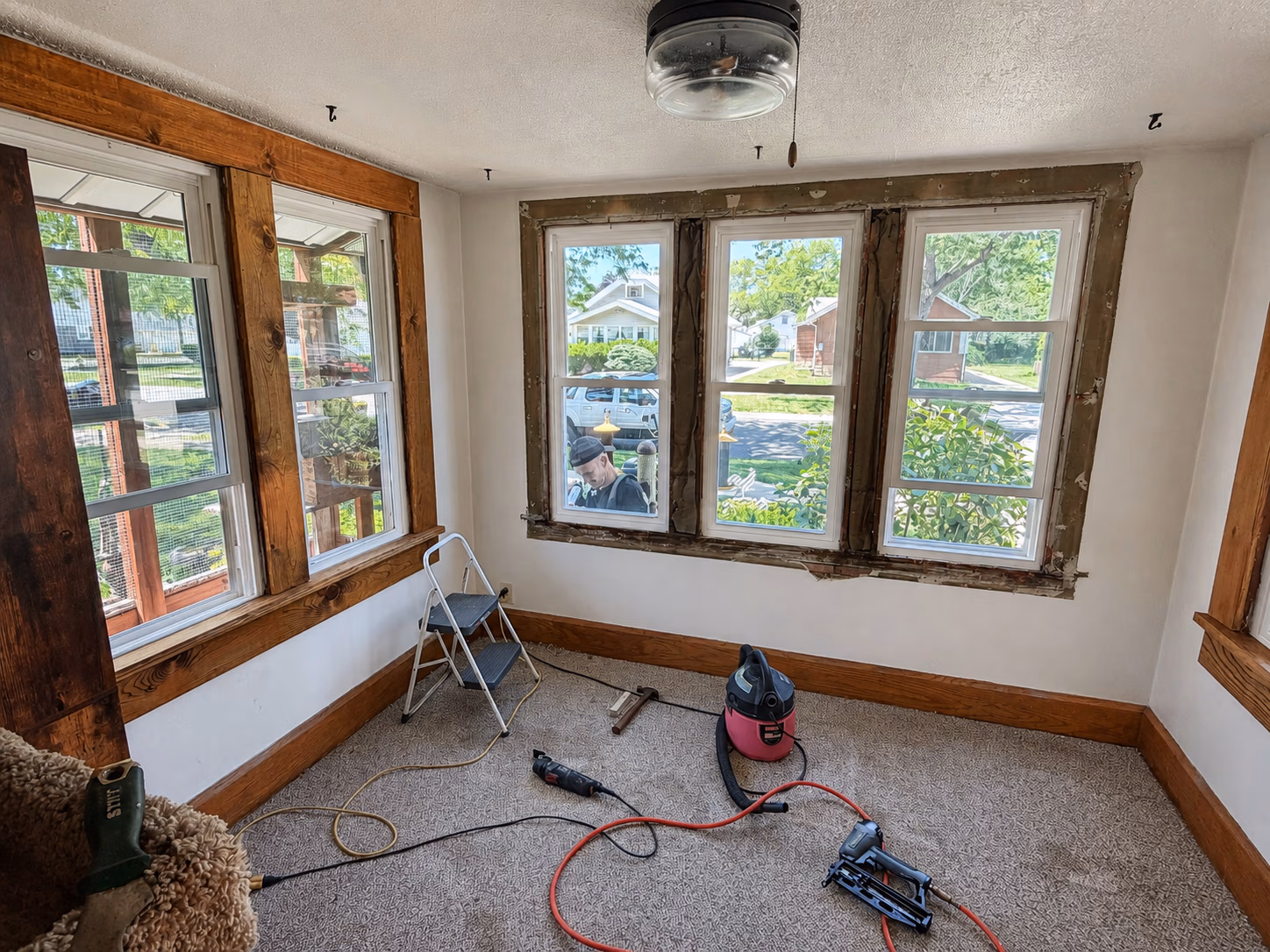 Room with carpet and untrimmed windows is being renovated with tools and ladder inside.
