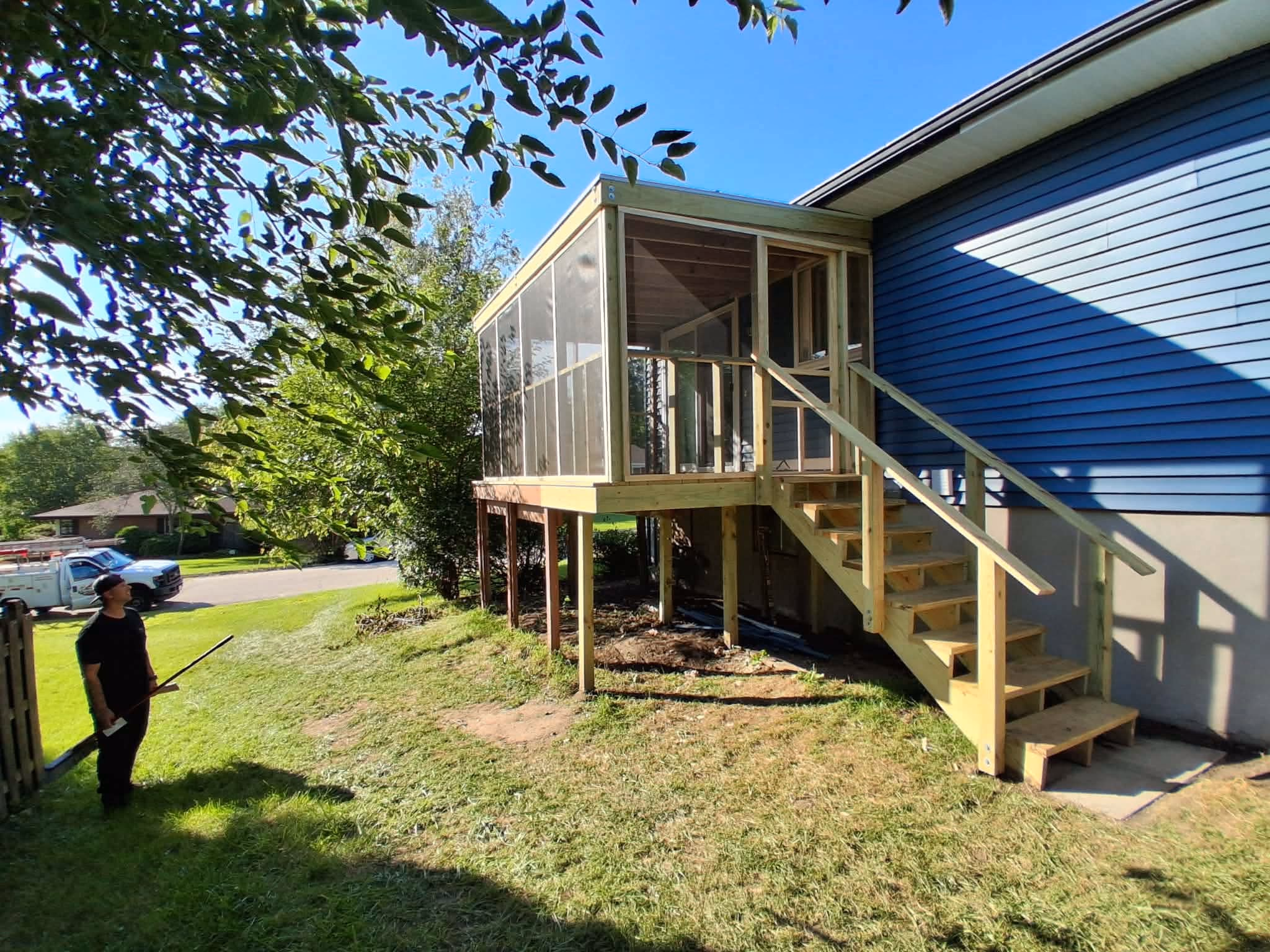 Man standing on grass looking at elevated wooden screened porch attached to blue house.