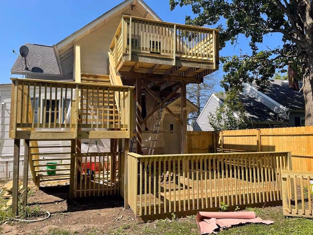 Multi-level wooden deck attached to the back of a house with fenced railings and stairs, under a clear blue sky.