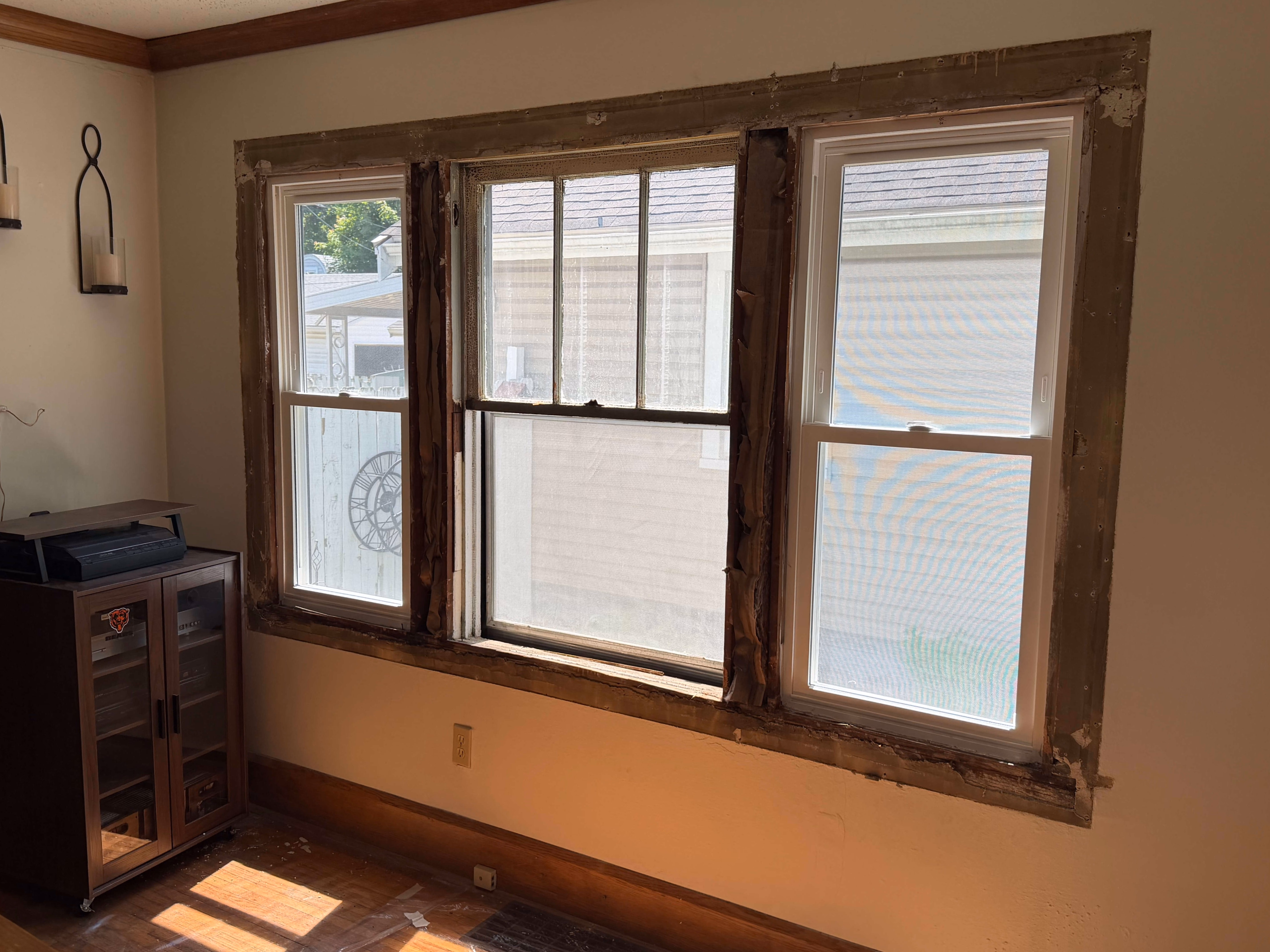 Three windows in a room with peeling paint and exposed trim around frames under renovation.