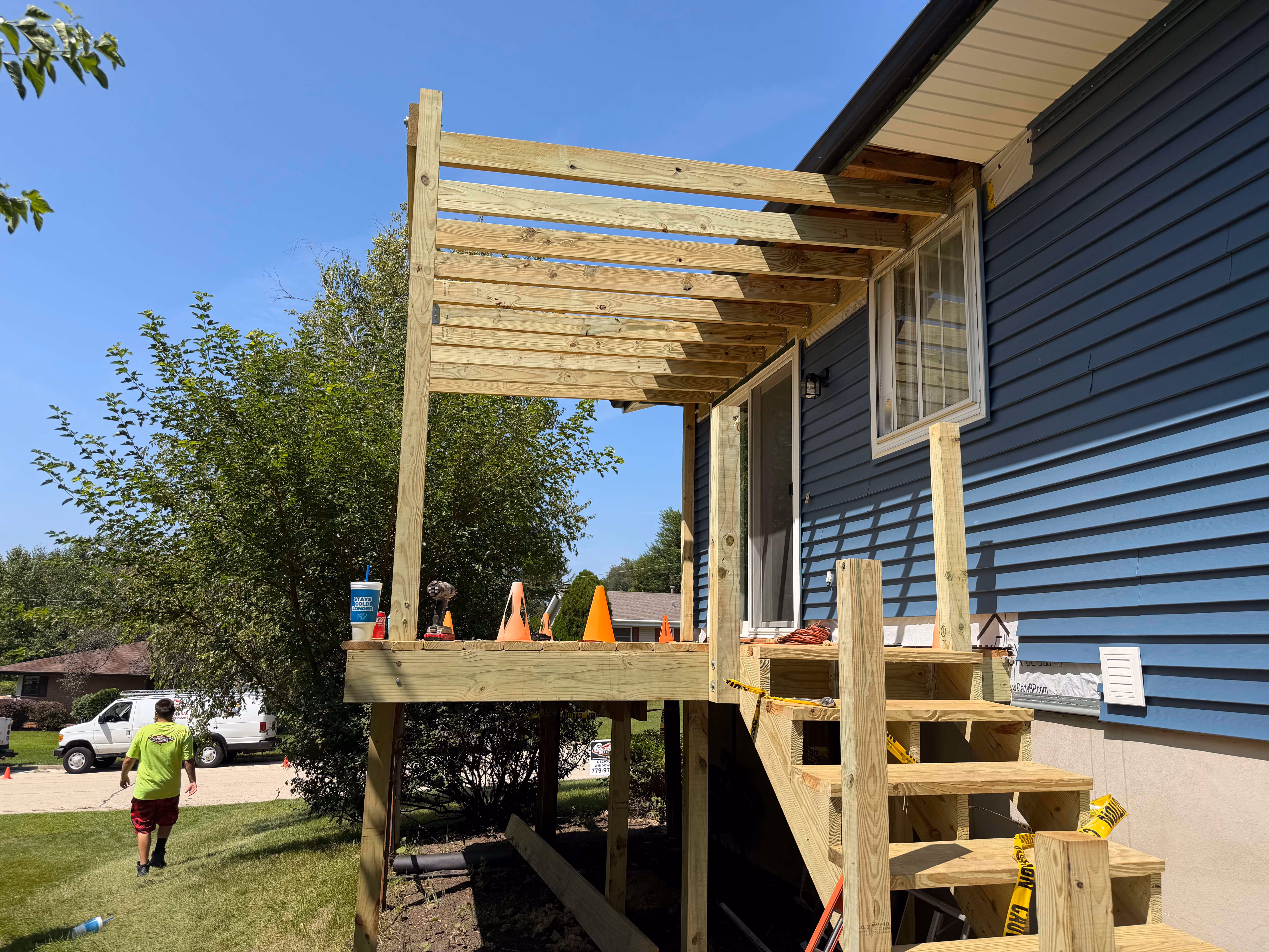 Wooden deck under construction attached to blue-sided house with stair frame but no railing yet.