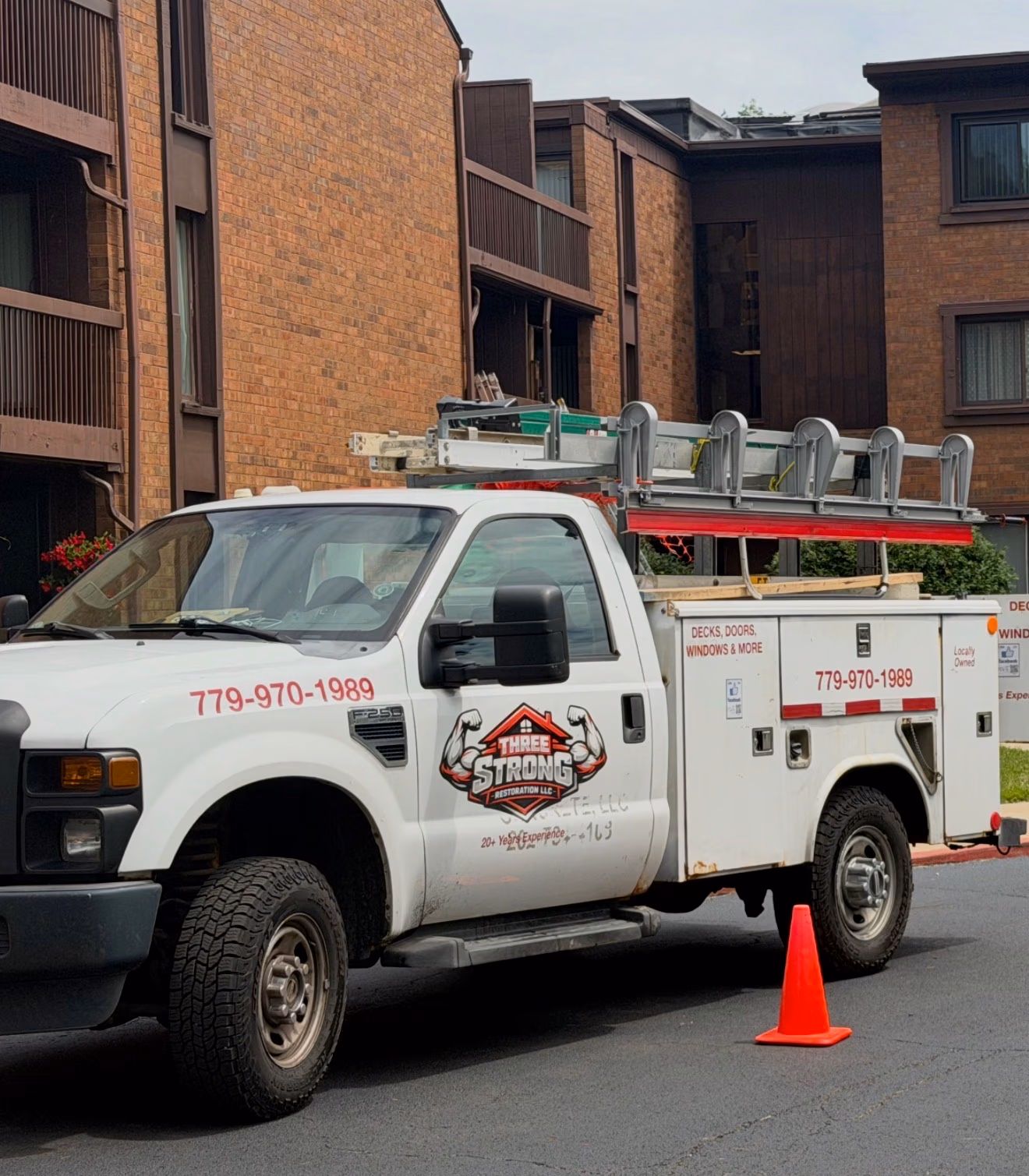 White work truck with ladders on top and Three Strong Restoration logo parked by brick buildings.