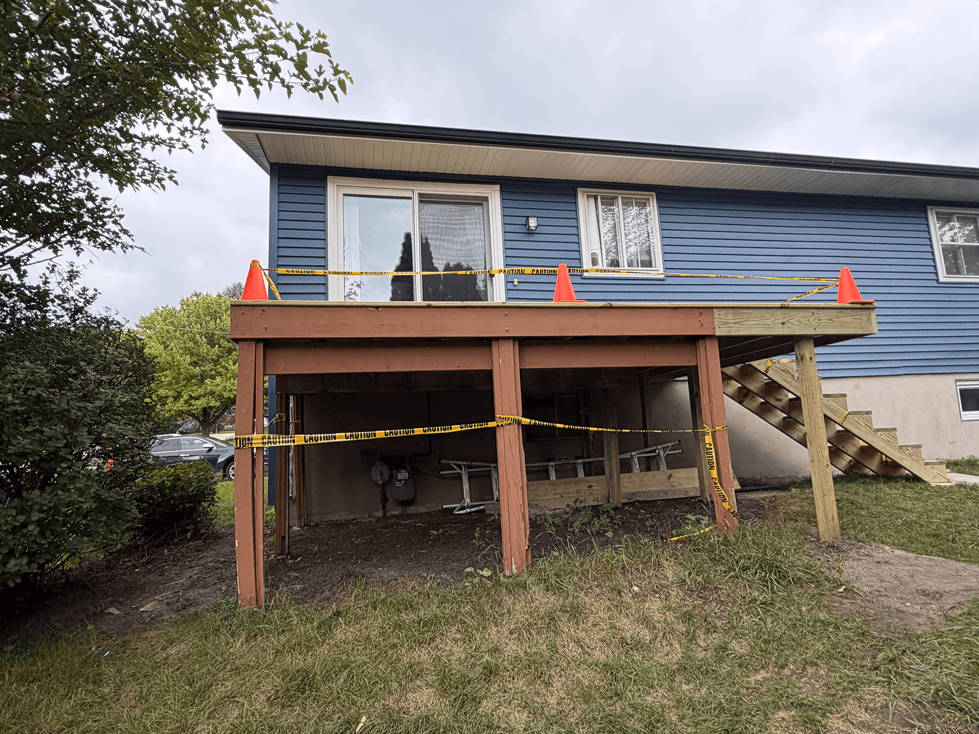 Wooden deck attached to a blue house, surrounded by caution tape and orange safety cones.